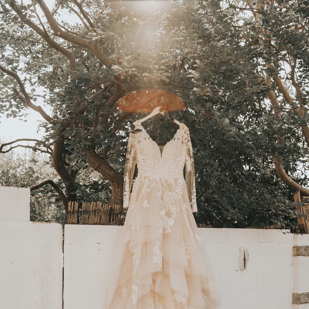A wedding dress with large layered tulle skirt hangs from a tree.