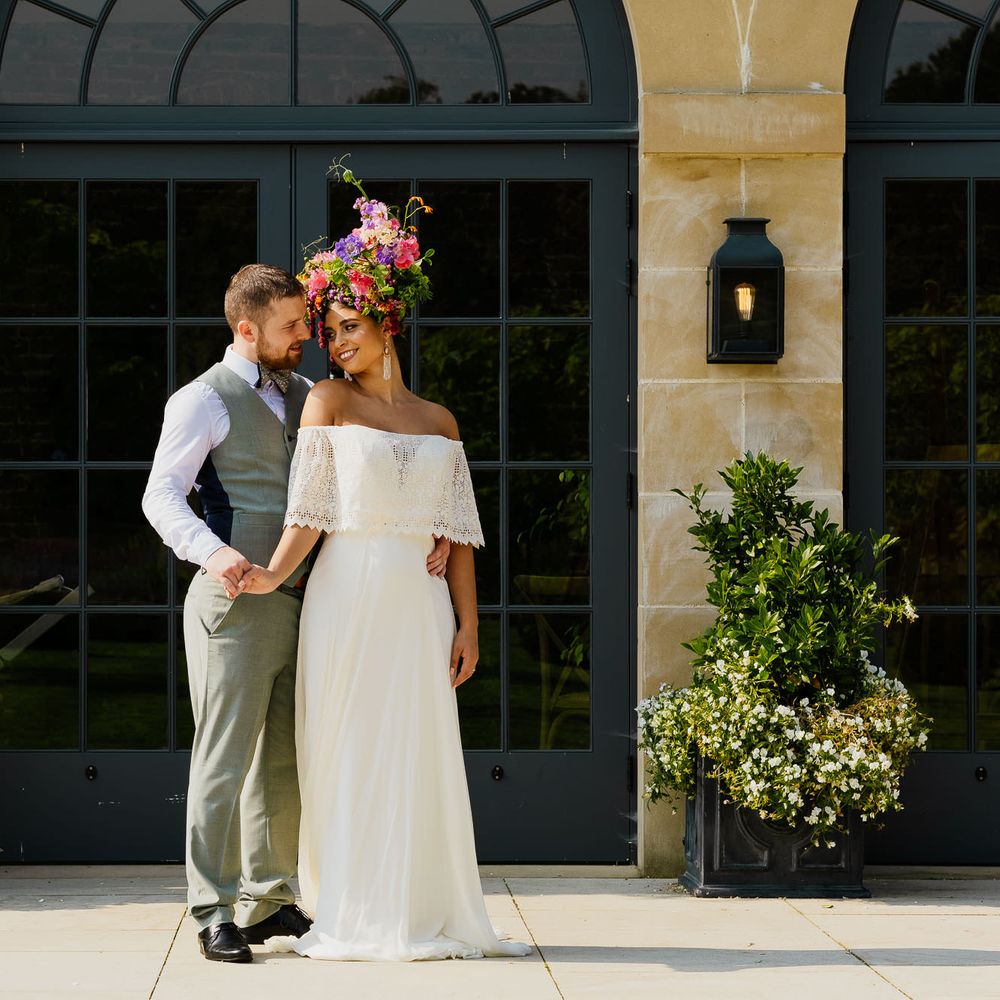 Bride in a strapless wedding dress with lace layer wearing a colourful wildflower crown standing outside The Fig House at Middleton Lodge 