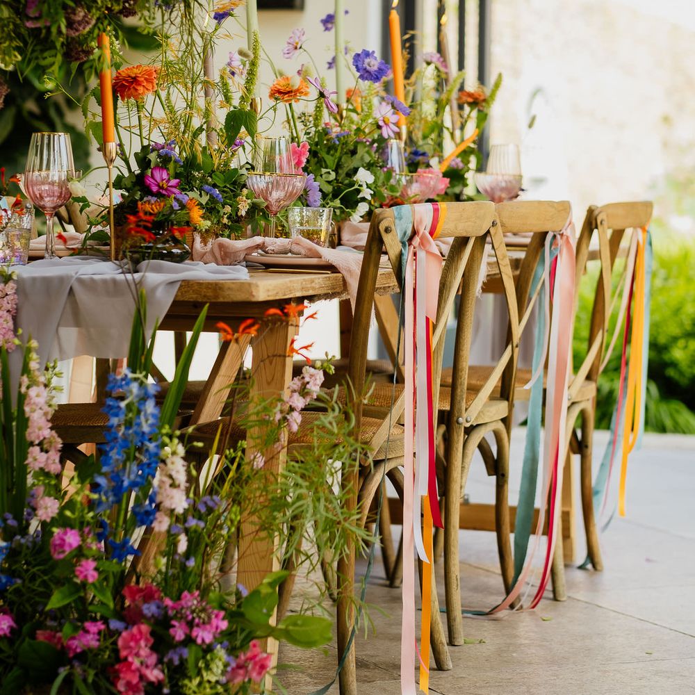 Fiesta theme wedding table decor with ribbon chair backs, wildflower centrepieces, taper candles and coloured glassware 