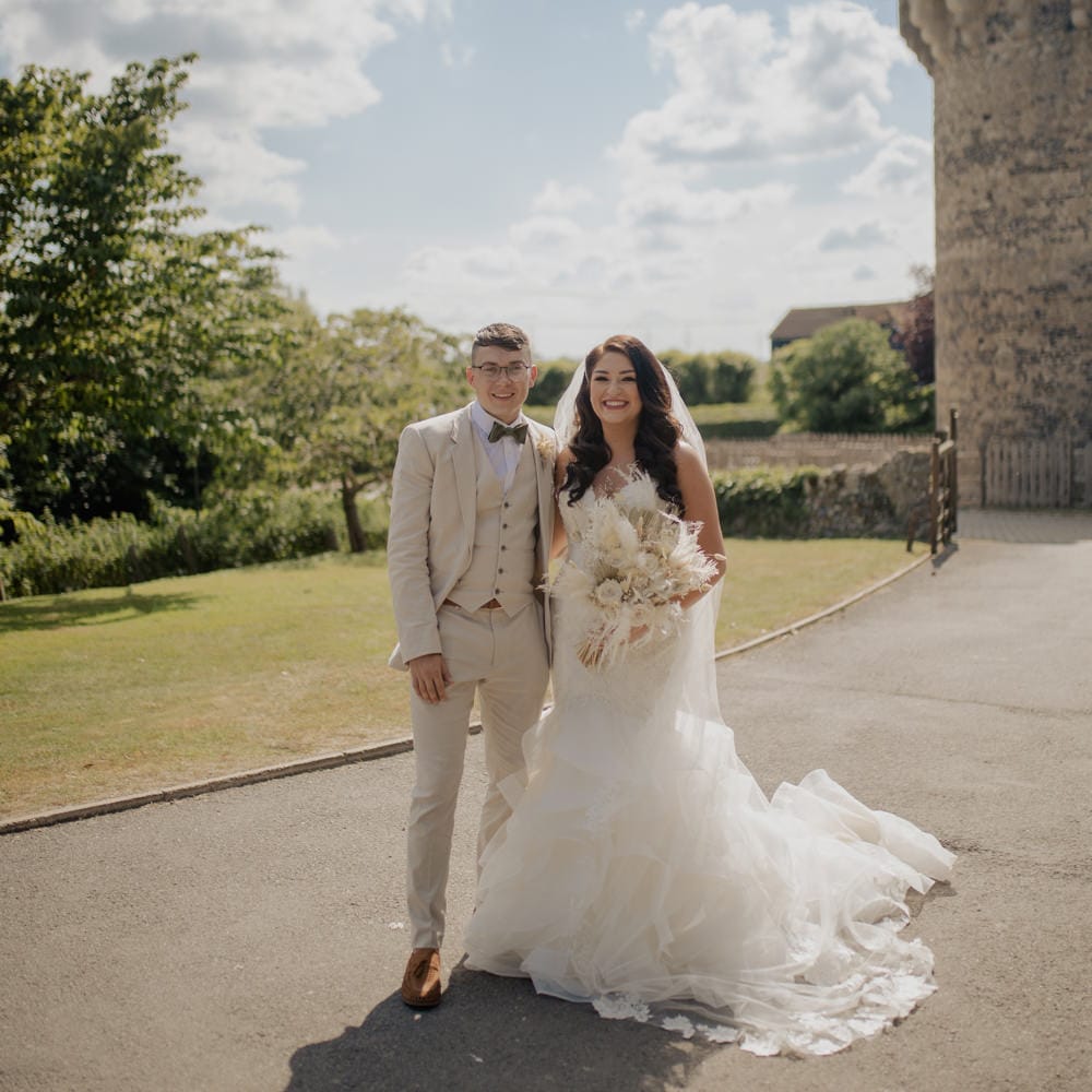 Portrait of the Bride in a Mori Lee wedding dress and the groom in a beige suit outside their Cooling Castle Barn wedding venue 