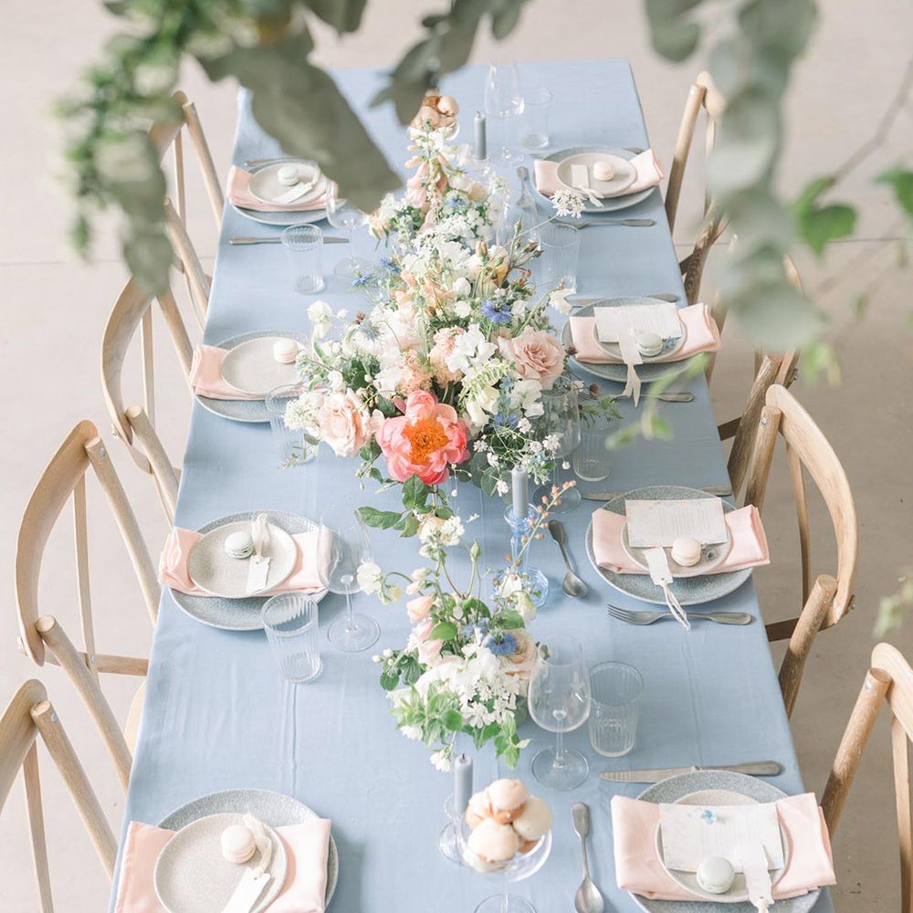 Ariel view of a wedding reception table with blue table cloth and tableware, pink napkins, macaroon favours and pastel floral arrangements 