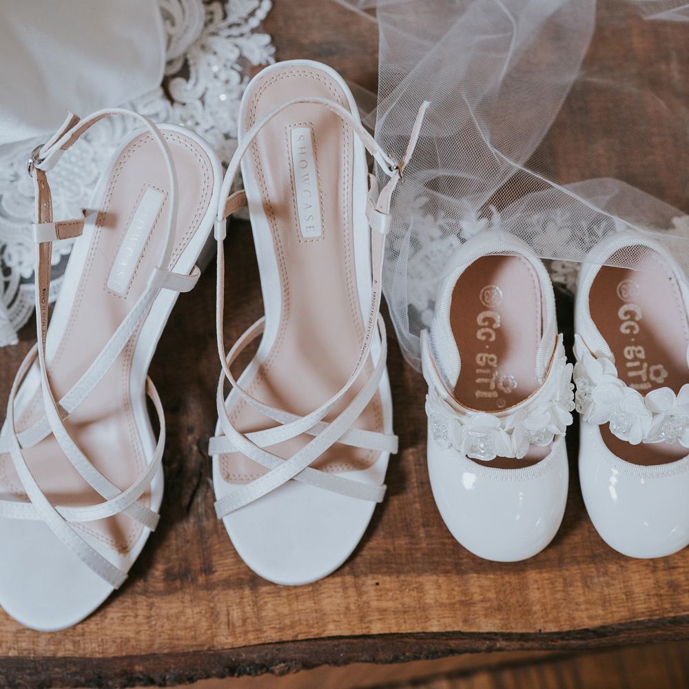 White strapped heeled sandals next to chide white sandals with strap next to wedding dress and veil at Tythe Barn wedding with barn wedding flowers