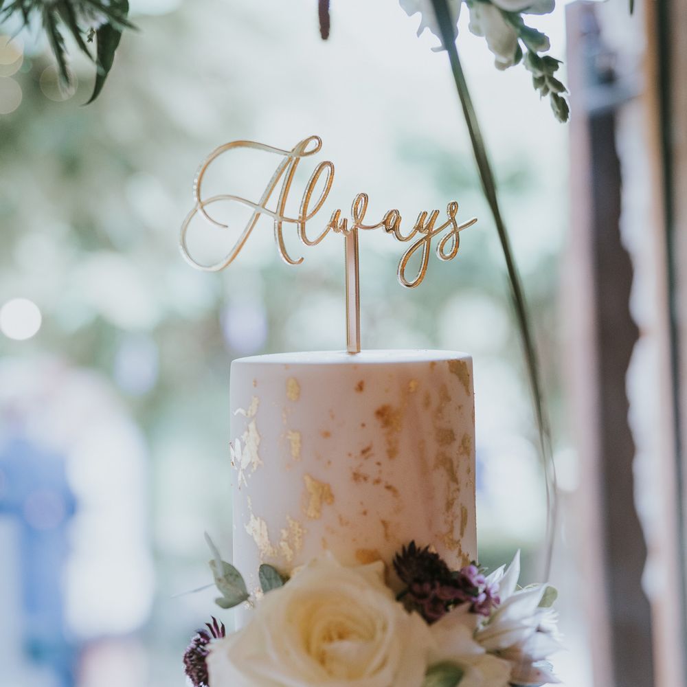 White wedding cake with gold leaf details, white rose decor and cake topper reading 'Always' at Tythe Barn wedding with barn wedding flowers
