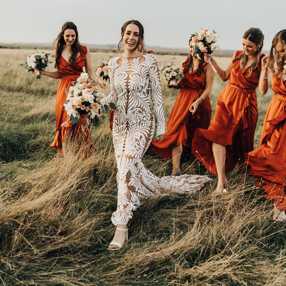 Bride in long lace boho wedding dress smiles with bride maids in Satin bridesmaid dresses in open natural setting