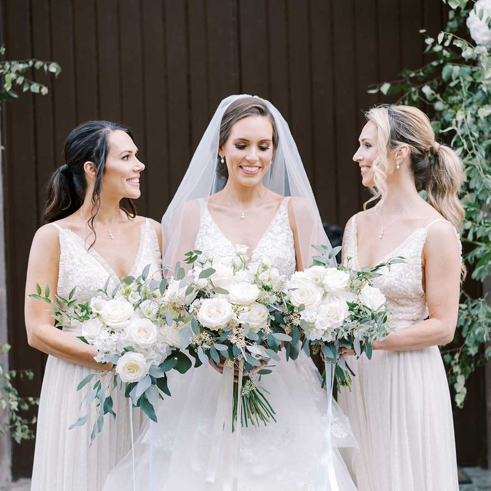 Bridal party portrait with bridesmaids in white dresses, and the bride in a Martina Liana wedding dress holding white rose and eucalyptus bouquets 