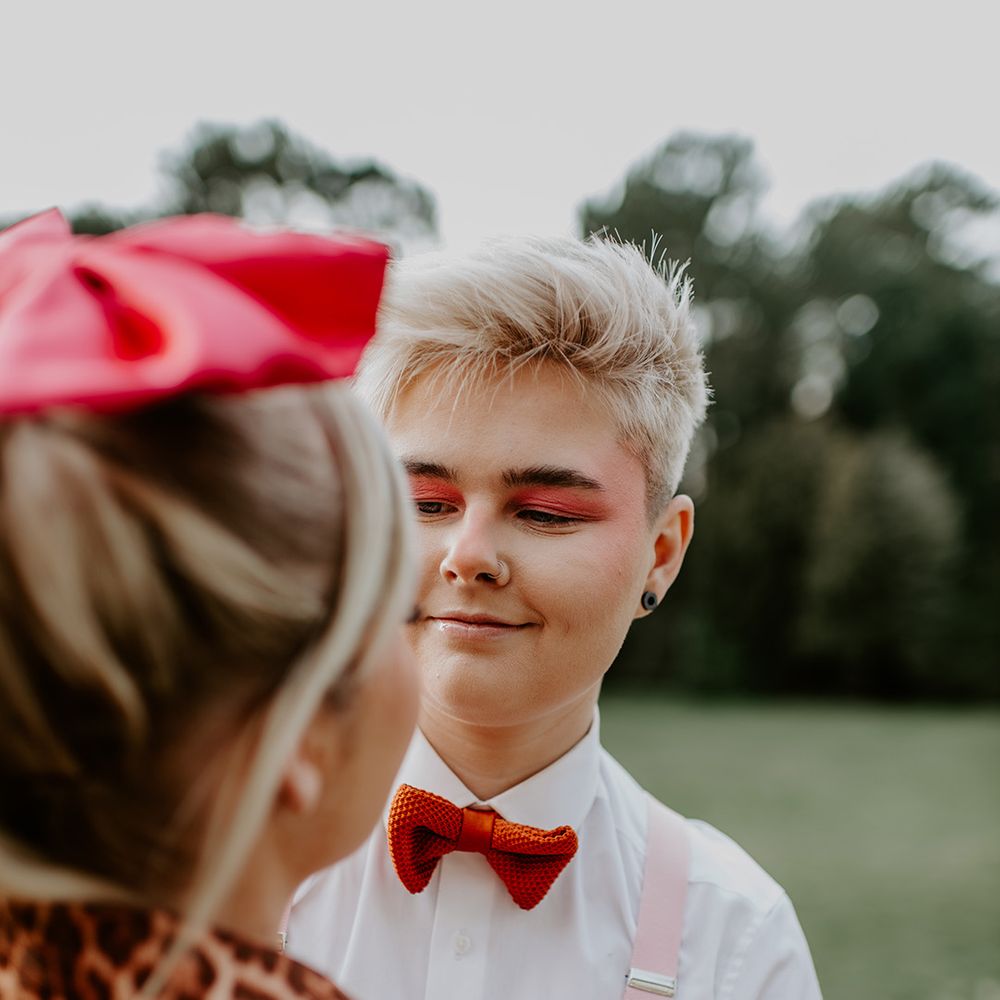 LGBTQI+ wedding with bride with short hair wearing braces and bow tie with red eyeshadow makeup 