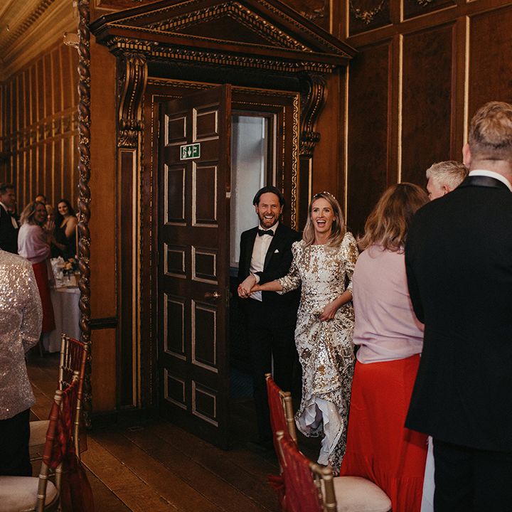 Bride walks into reception room with her groom whilst wearing sequinned Abigail Of Gardenia gown