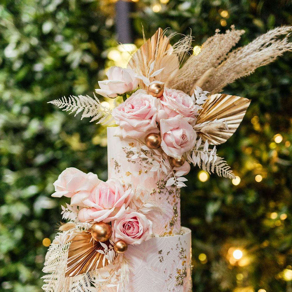 Two tier wedding cake with dried palm leaves, gold gilt and pink flower decor 