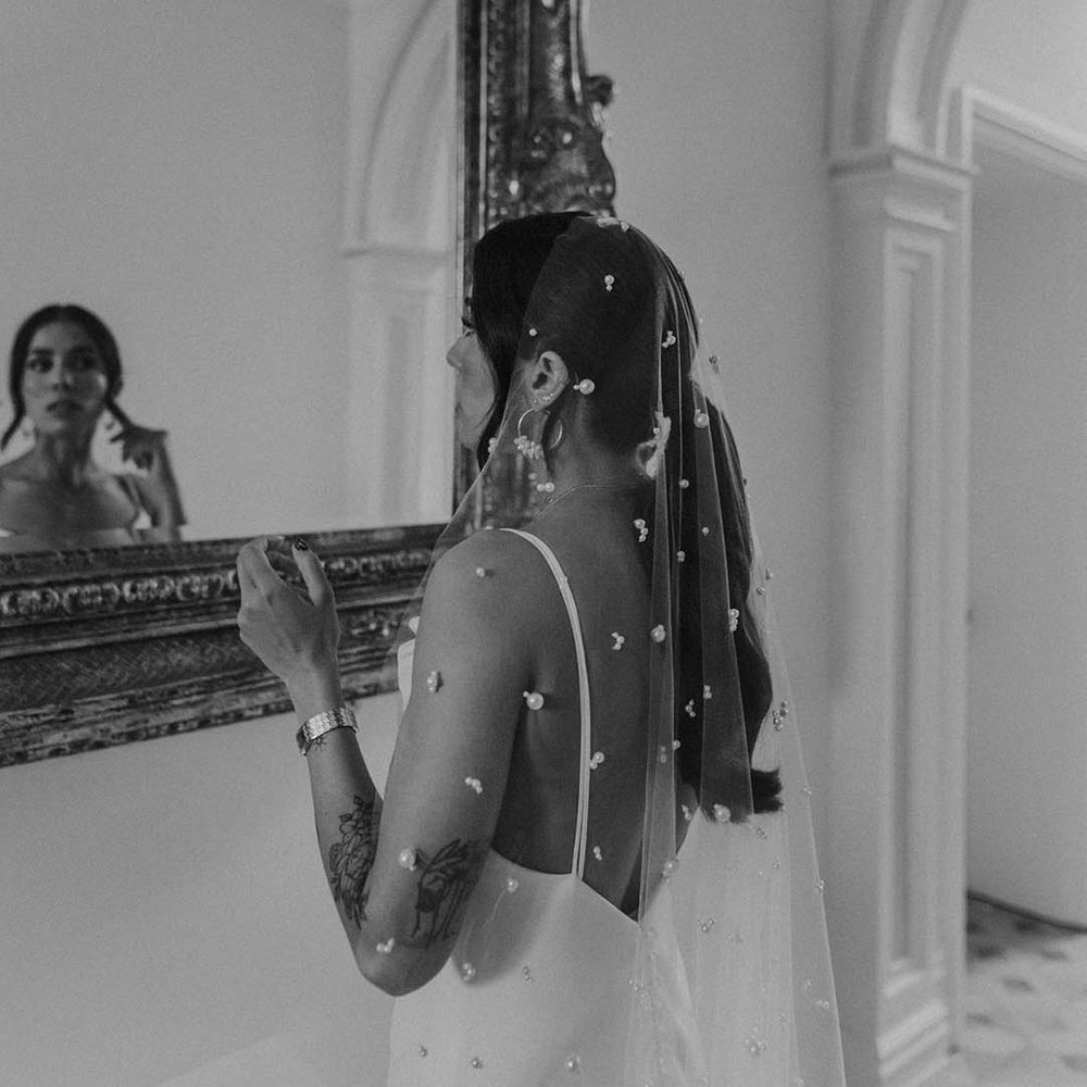 Bride in a satin wedding dress with spaghetti straps wearing a long cathedral length veil with pearl embellishment 