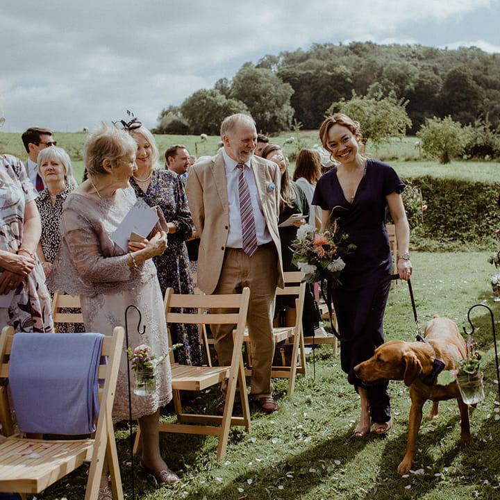 Bridesmaid in navy blue dress walks pet dog down the aisle 