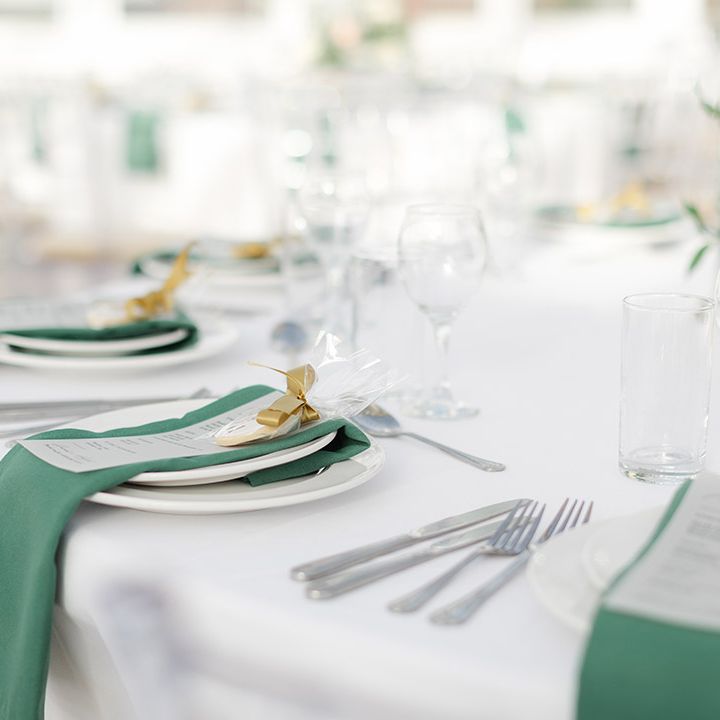 Green napkins placed on white plates complete with gold ribbon for reception at the Isla Gladstone Conservatory