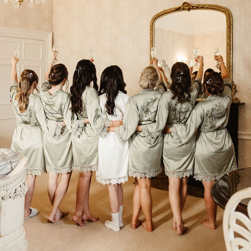 Bride wears white silk short dressing gown alongside her bridesmaids who wear matching dressing gowns in sage green