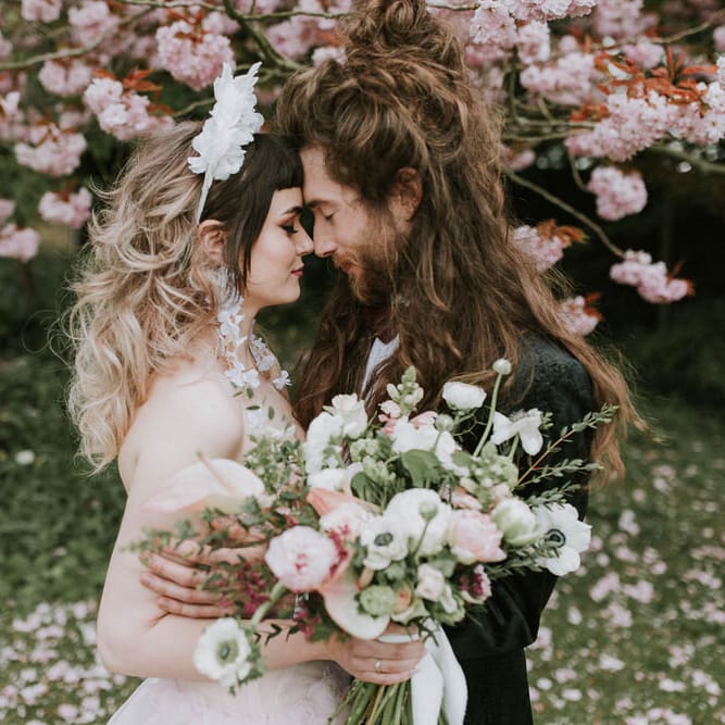 Couples' portrait under a blossom tree with bride in a white 3D flower headband and pink wedding dress and groom a black suit. 