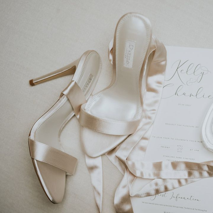 White satin ribbon Dune wedding shoes with the bride's perfume and traditional wedding invitation