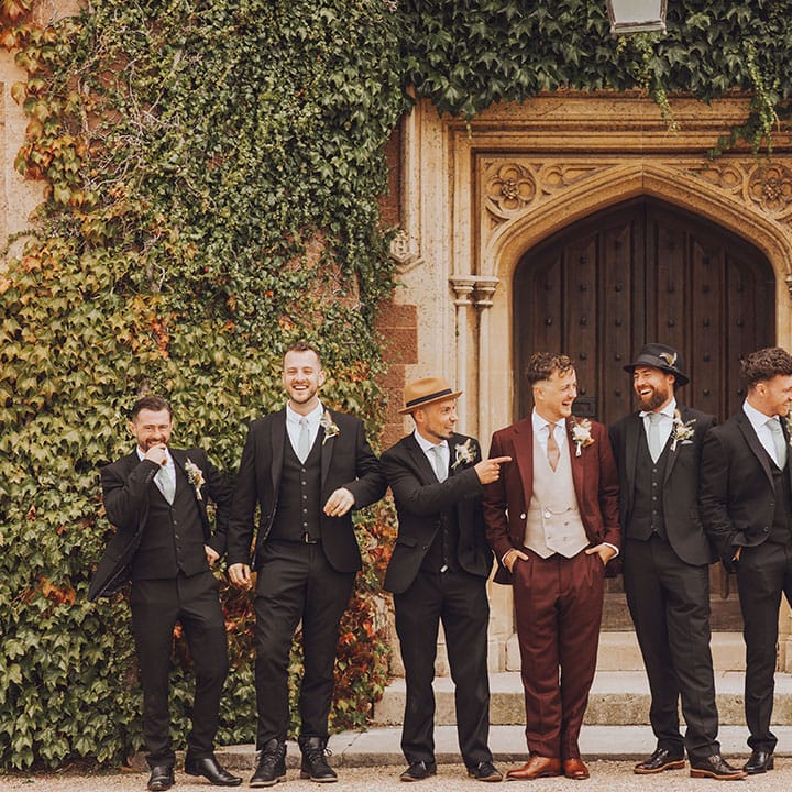 Groom in maroon suit stands outdoors with his groomsmen in black suits and pale blue ties