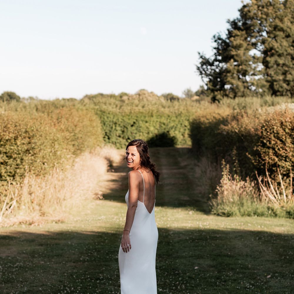 Bride wears simple silk low back wedding dress and her brown hair in low up do with loose curls 