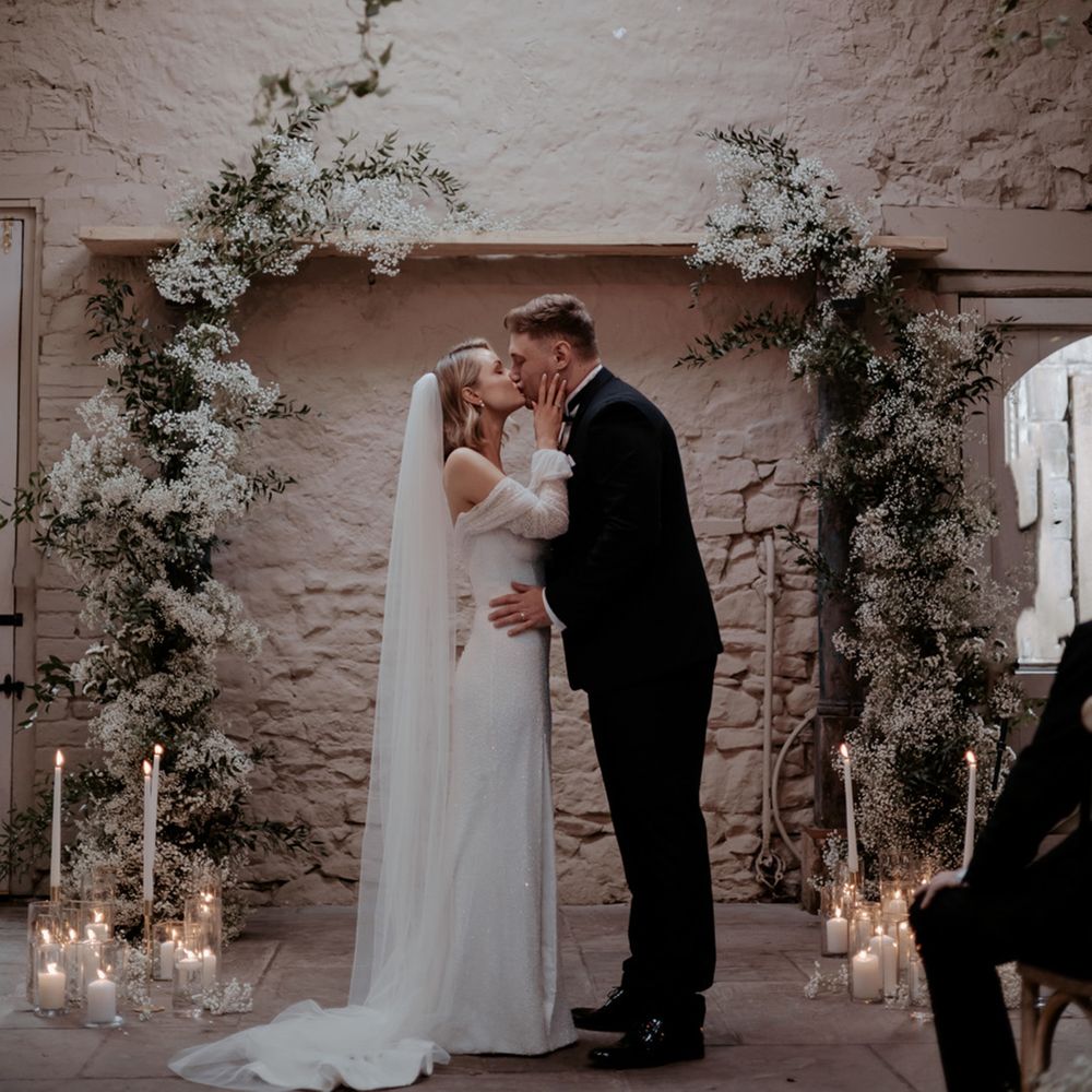 The bride and groom kiss standing in between the gypsophila flower columns at their ceremony 