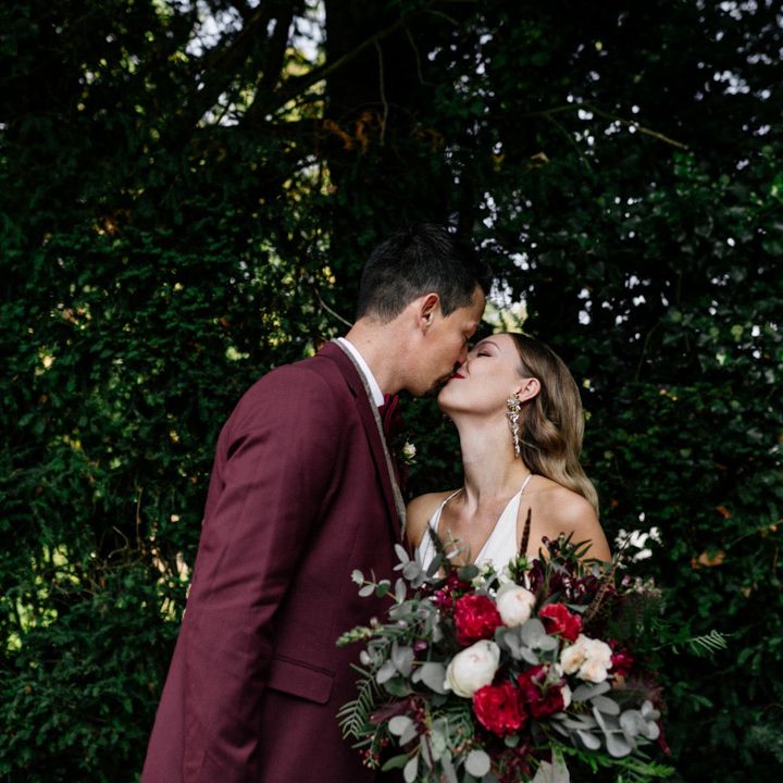 Groom in burgundy jacket kissing his bride