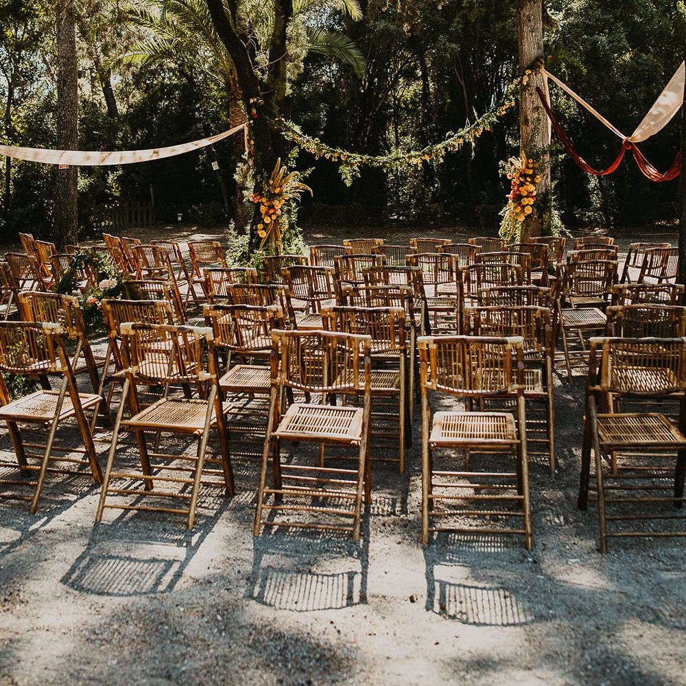 Outdoor forest wedding ceremony with wooden chairs and floral garland 