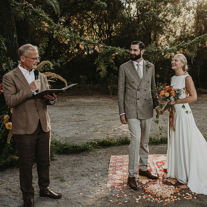 Bride and groom standing on a moroccan rug during woodland wedding ceremony 