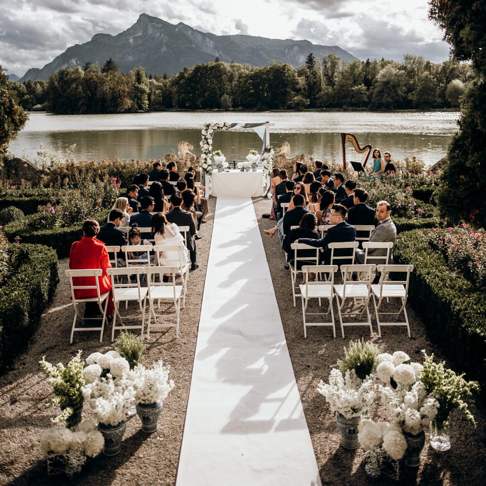 Outdoor wedding ceremony by a lake with wooden frame altar decorated in drapes and flowers 