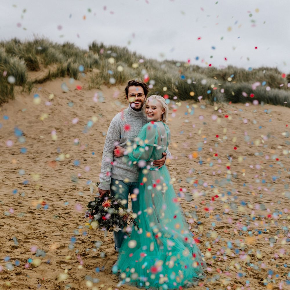 Colourful confetti cannon moment for a beach elopement with bride in a sheer wedding dress and the groom in jumper and jeans 