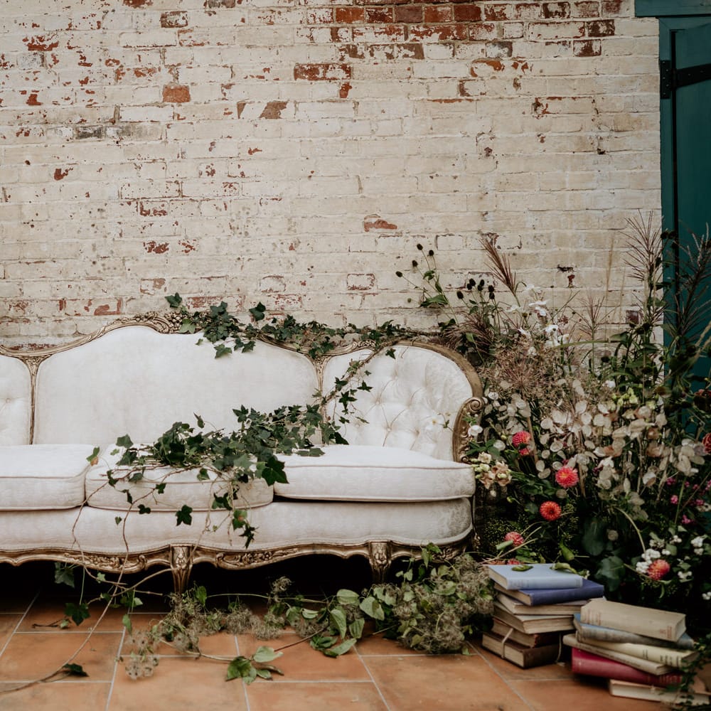 White vintage sofa with gold guilt design surrounded by wildflower arrangements in Our Beautiful Glasshouse in Sussex