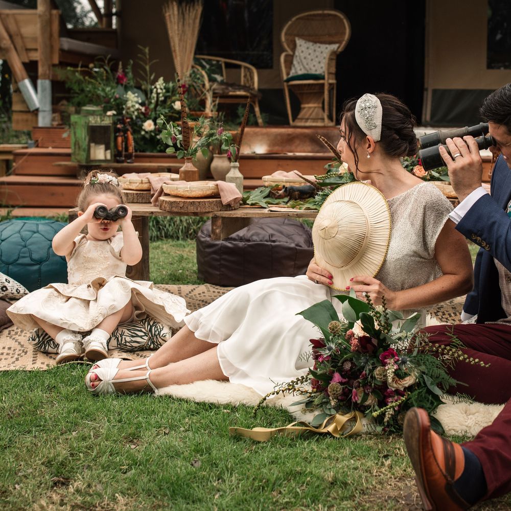 Bride & groom sit with little girl on the floor who plays with binoculars 