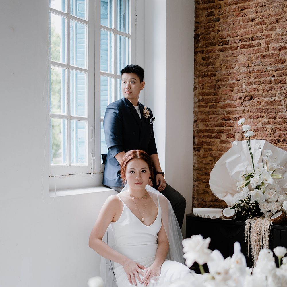 Bride in a navy suit jacket and bride in a minimalist wedding dress sitting at their all white intimate tablescape 