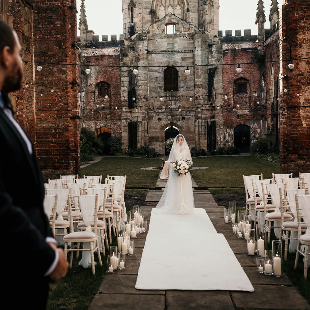 Groom in a black tuxedo standing at the altar waiting for his bride to walk down the aisle on a white carpet 