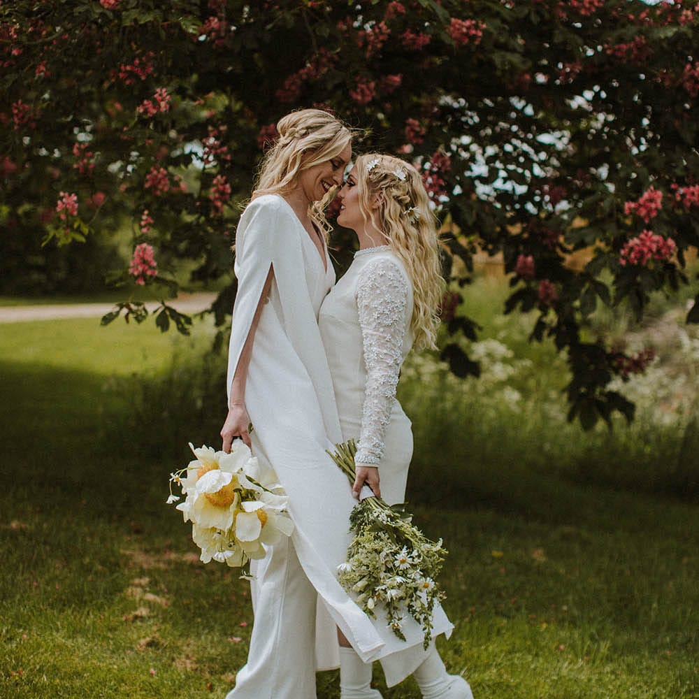 Intimate portrait of two brides holding a white peony and giant daisy bouquet with flowers in their hair 
