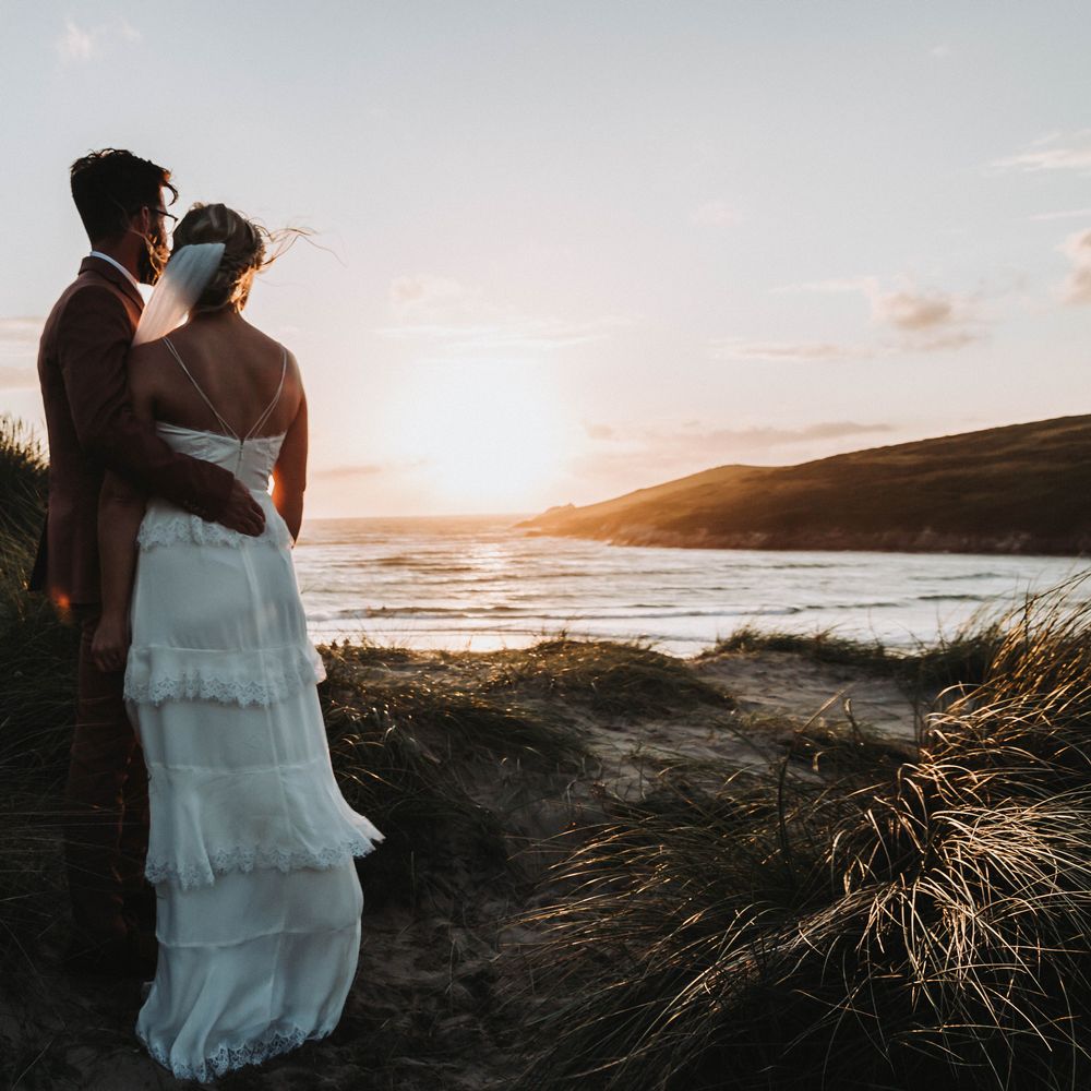 Bride & groom watch the sunset with one another on the beach together in Cornwall on their wedding day