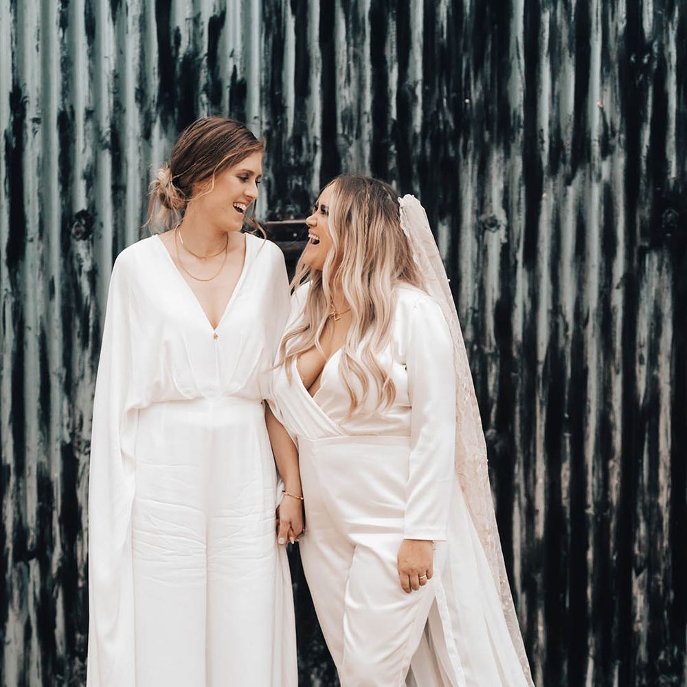 Brides look lovingly at one another as they stand together for couples portraits 