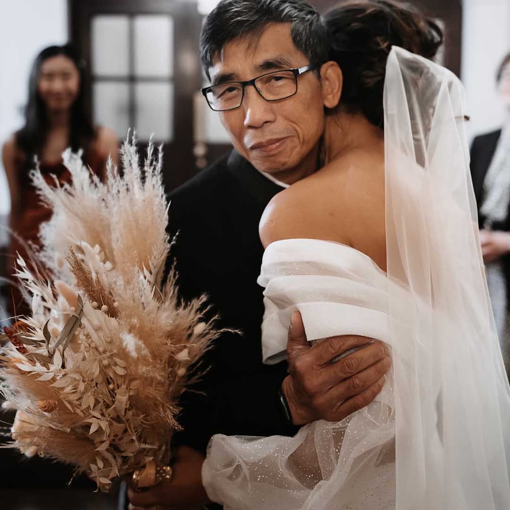 Father of the bride cuddles her as the sparkles shine in her detailed sleeves