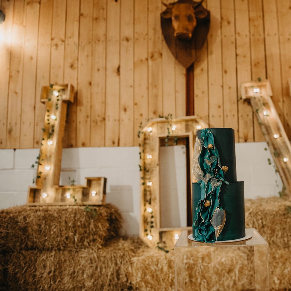 Big wooden letters spelling 'LOVE' on hay bales and blue two tier wedding cake for rustic farm wedding