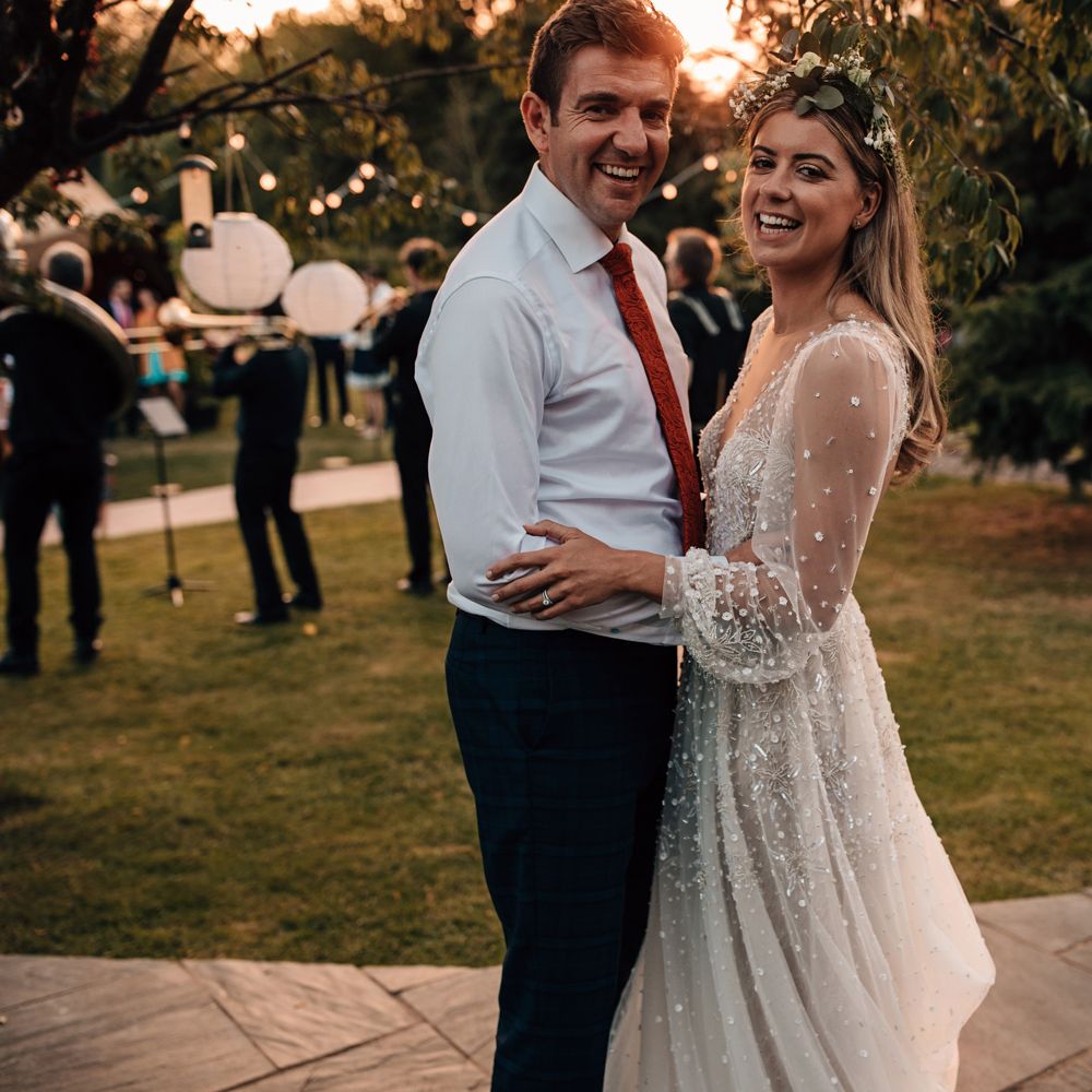 Bride in mesh long sleeve wedding dress and boho flower crown smiles whilst dancing with groom in white shirt during golden hour at tipi wedding 