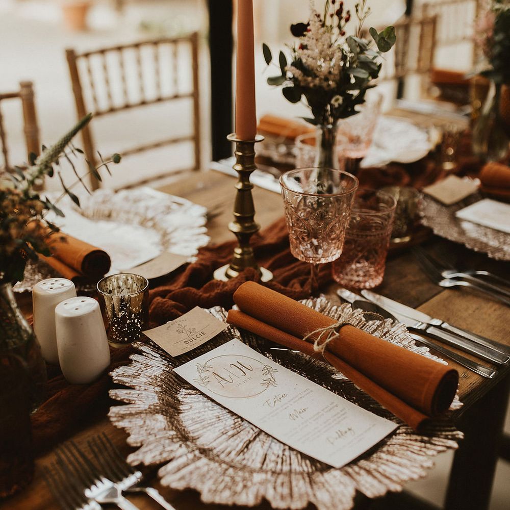 Beautiful wedding table place setting with rust napkins and gold candlesticks