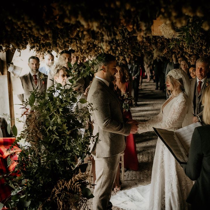 Autumnal wedding ceremony at Lyde Court with groom in a wool suit exchanging vows with his bride in a lace wedding dress with long sleeves
