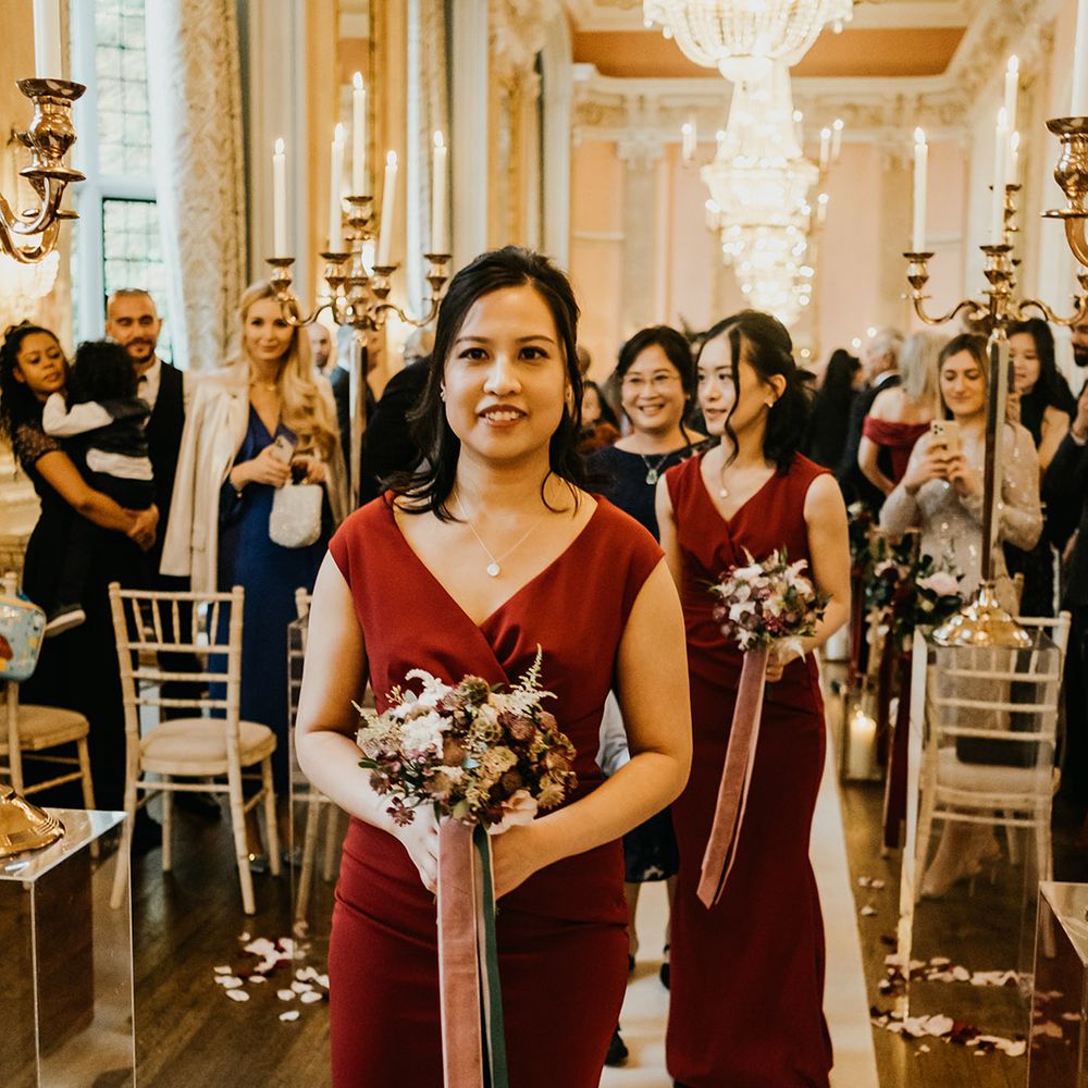 Bridesmaid in burgundy dress walks down the aisle at Danesfield House