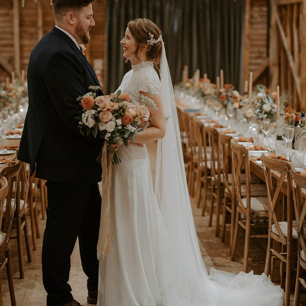 Bride clutches blush and orange bouquet as she looks at husband