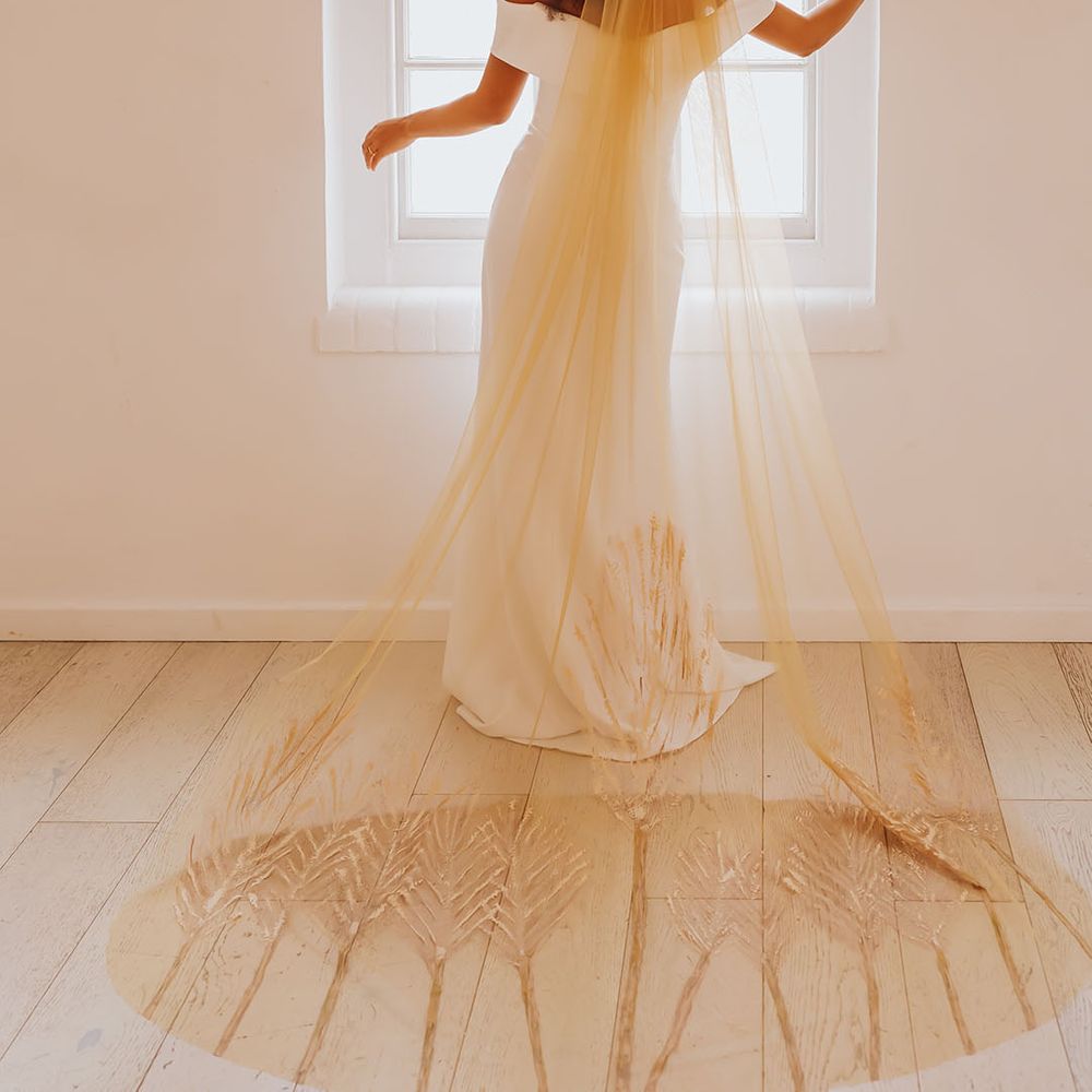 Black bride in an off the shoulder wedding dress with afro hair wearing a golden patterned wedding veil 
