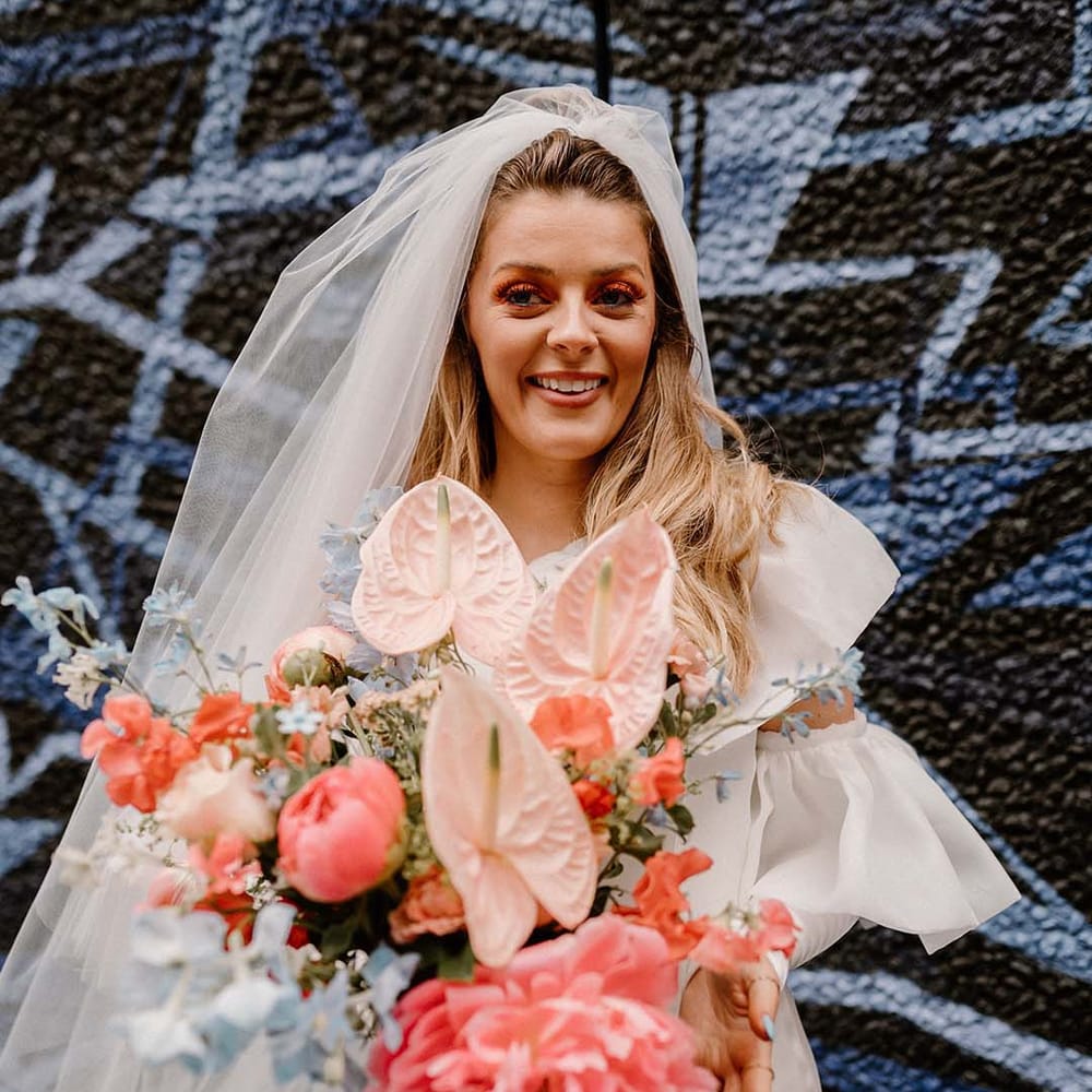 Fun wedding elopement with bride holding a coral pink and blue wedding bouquet with peonies, anthuriums and delphiniums