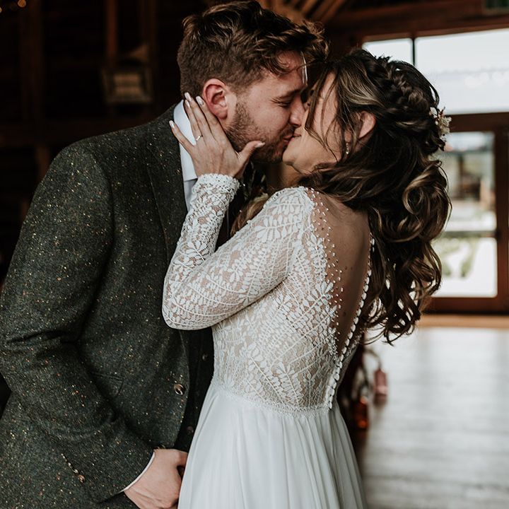 Groom in green wool suit shares first kiss as a married couple with the bride in lace patterned long sleeve top 