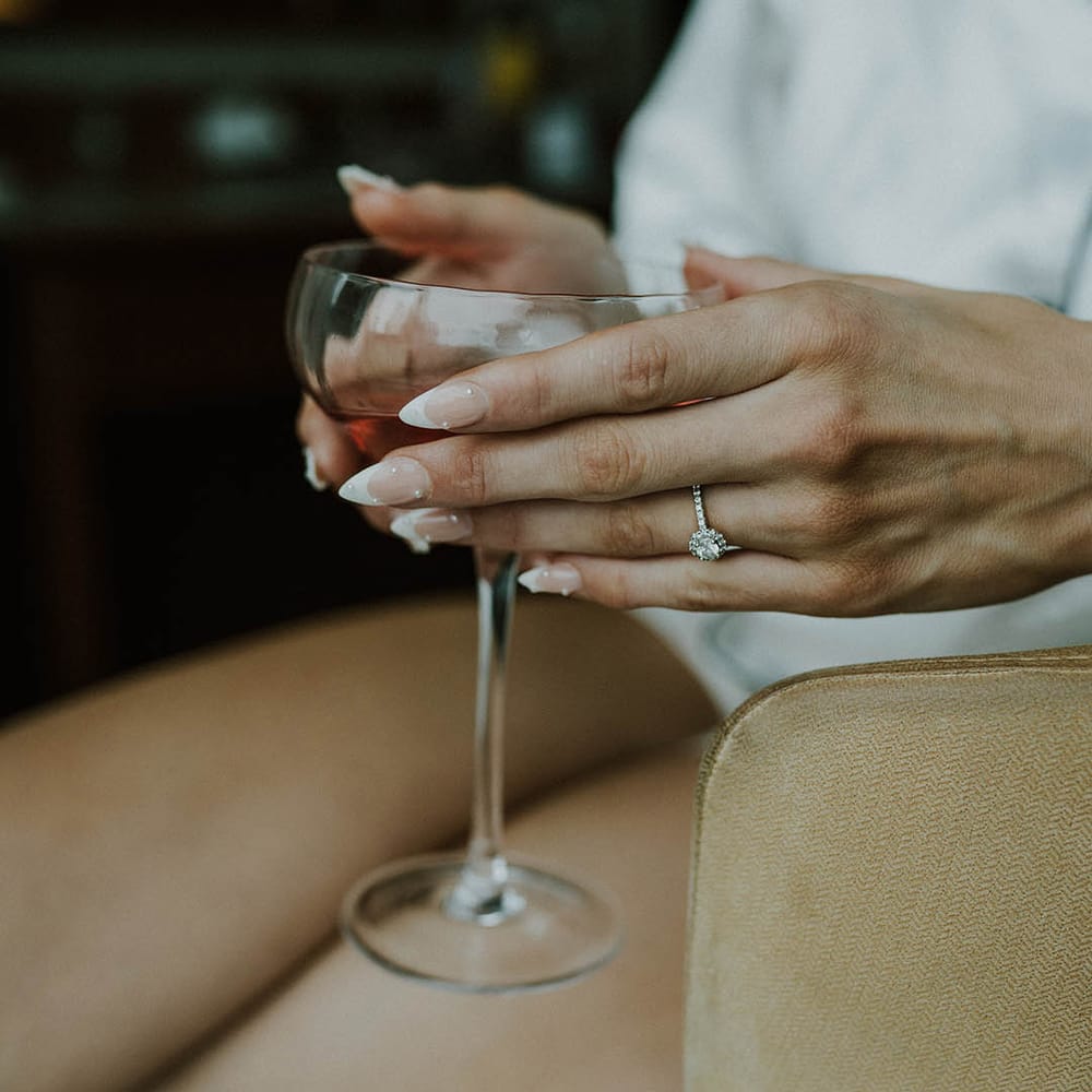 Bride with almond shape French tip nails with pearls holding cocktail glass with pave round diamond engagement ring 