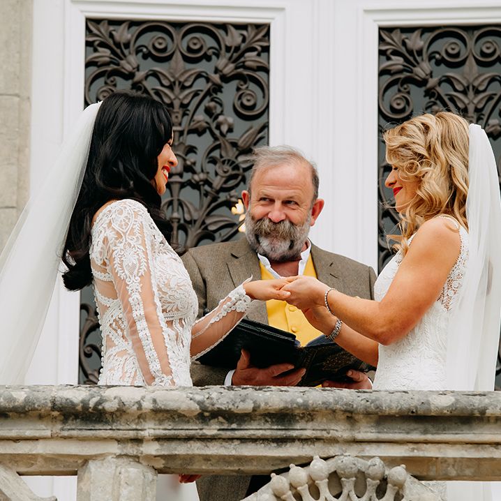 Bride with blonde hair with red lipstick places wedding band on the bride's hand 