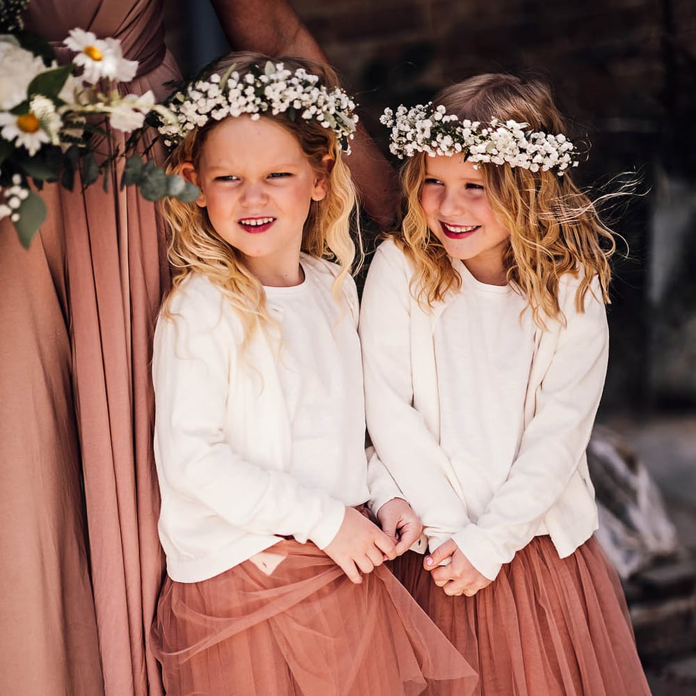 Flower girls with white flower crowns and pink tulle skirts with white cardigans 
