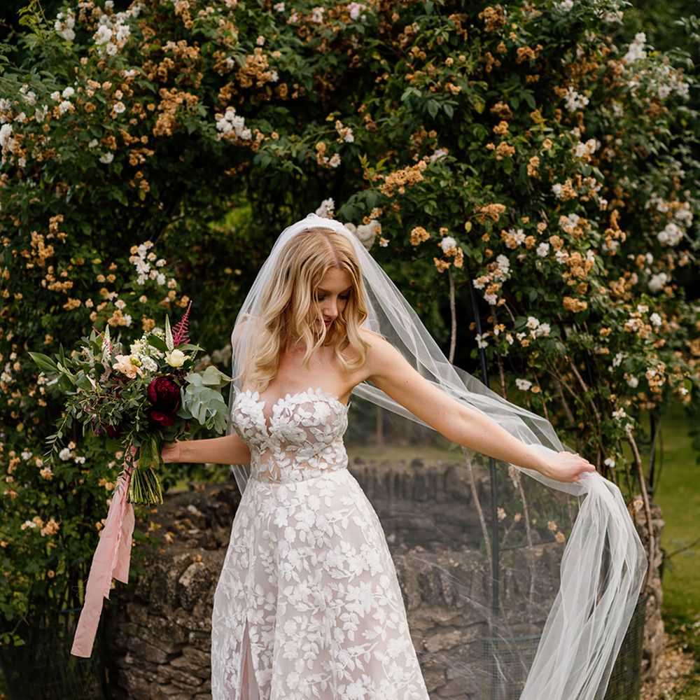 Bride holding red and white wedding bouquet tied with pink ribbon with veil and strapless lace wedding dress 