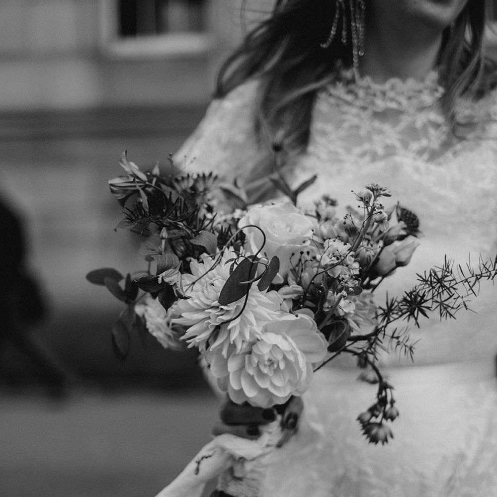 Bride wears bow styled statement earrings whilst carrying sustainable floral bouquet 
