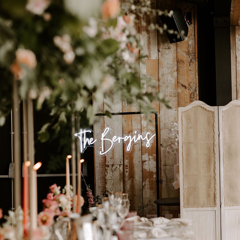 Personalised neon wedding sign hangs in front of wooden wall 