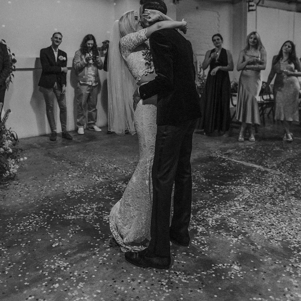 Bride in boho two piece lace bridal outfit and groom in dark tux with bowtie kissing at Hackney Studios wedding